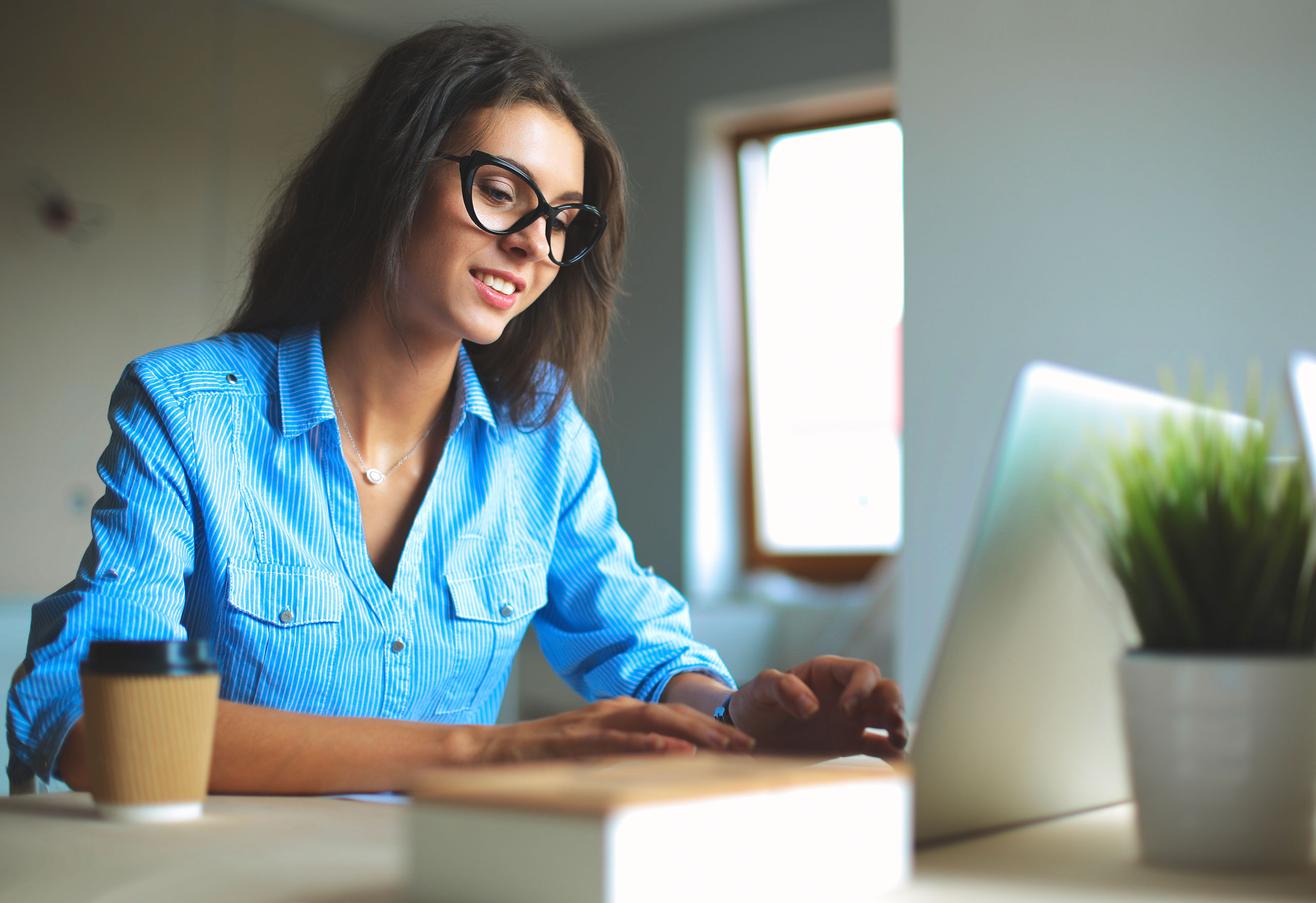 Woman in a blue shirt looking at financial reconciliation reports on a laptop.